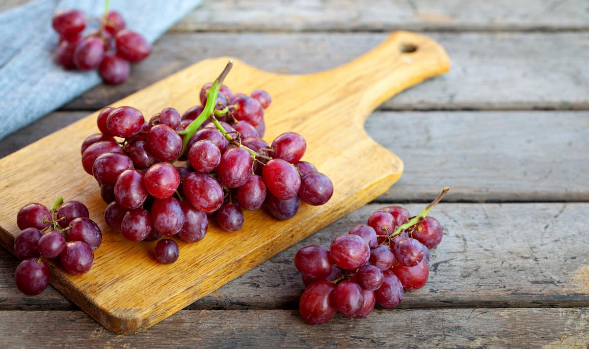 A bunch of fresh red grapes on a wooden chopping board on top of a old paneled table